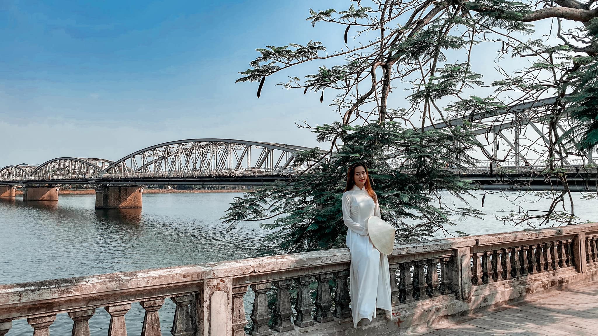 Em gái khi du lịch Huế trong bộ áo dài truyền thống ngồi bên sông Hương chụp ảnh